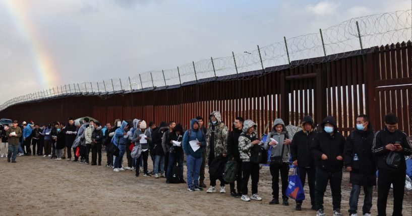 Asylum seeking migrants wait in line to receive donated food, with a rainbow in the distance, at a makeshift camp while awaiting processing by the U.S. Border Patrol in a file photo from November 2023 in Jacumba Hot Springs, California.