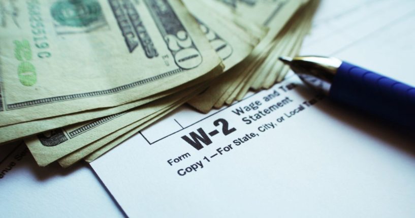 This stock image shows a stack of cash next to a W-2 form.