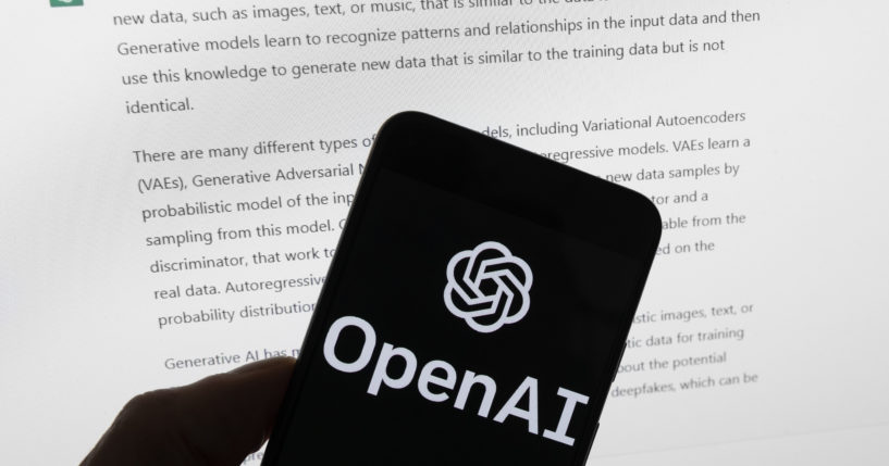 The Open AI logo is seen on a mobile phone in front of a computer screen displaying output from the company's ChatGPT software in Boston on March 21, 2023.