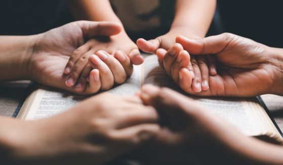 A mother and father and child holding hands in prayer over the family Bible.