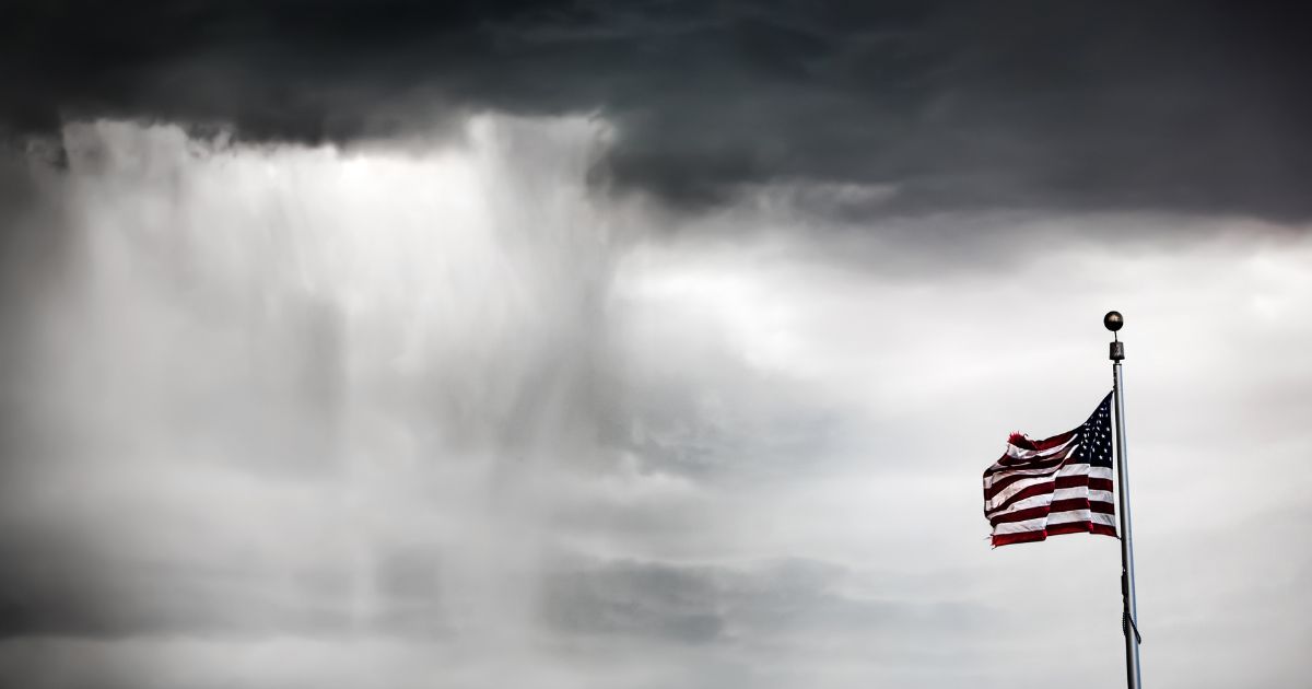 This image shows the American flag flying during a rain storm with dark clouds in background.