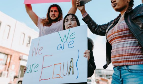 This image shows three adults standing outside buildings, holding up signs demanding equality.