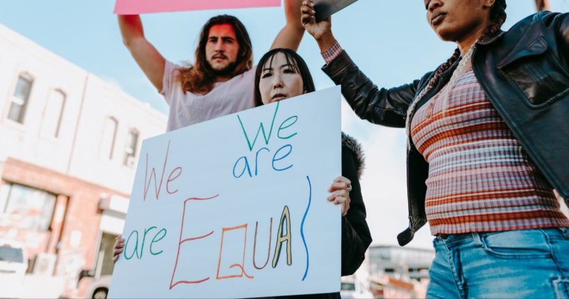 This image shows three adults standing outside buildings, holding up signs demanding equality.