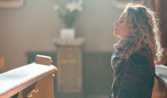 This image shows a young woman sitting on a pew, praying in the church.