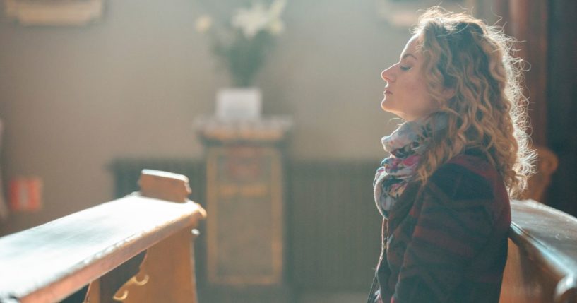 This image shows a young woman sitting on a pew, praying in the church.