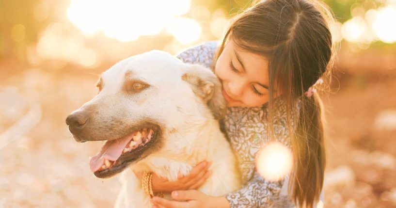 This image shows a young girl hugging a dog outside.