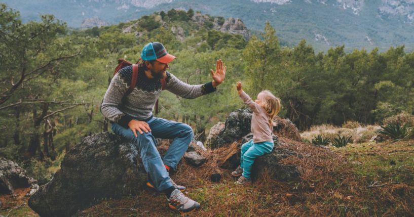 A father and daughter high-five in the mountains after hiking together.