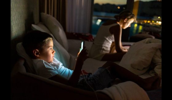 This Getty stock image shows a young boy on his phone, while his mother is on a laptop in the background.