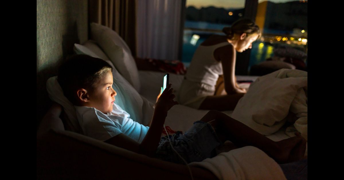 This Getty stock image shows a young boy on his phone, while his mother is on a laptop in the background.
