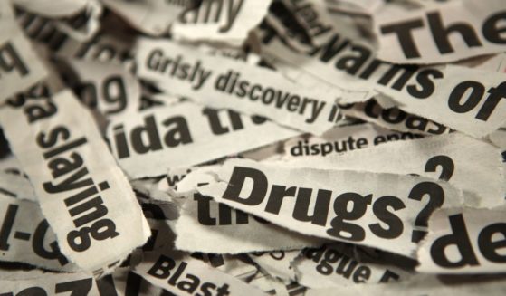 This image is a close up of a pile of newspaper headline clippings reading 'grisly discovery, slaying, drugs.'