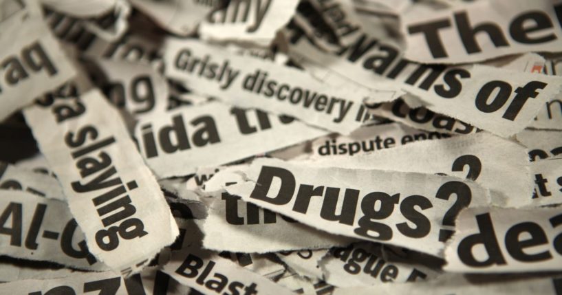 This image is a close up of a pile of newspaper headline clippings reading 'grisly discovery, slaying, drugs.'