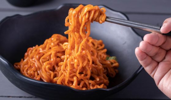 A stock photo shows Korean spicy instant noodles in a black bowl.