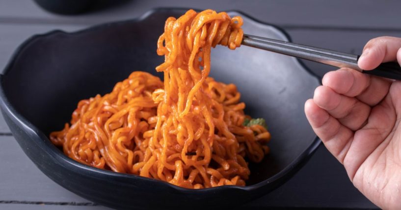 A stock photo shows Korean spicy instant noodles in a black bowl.