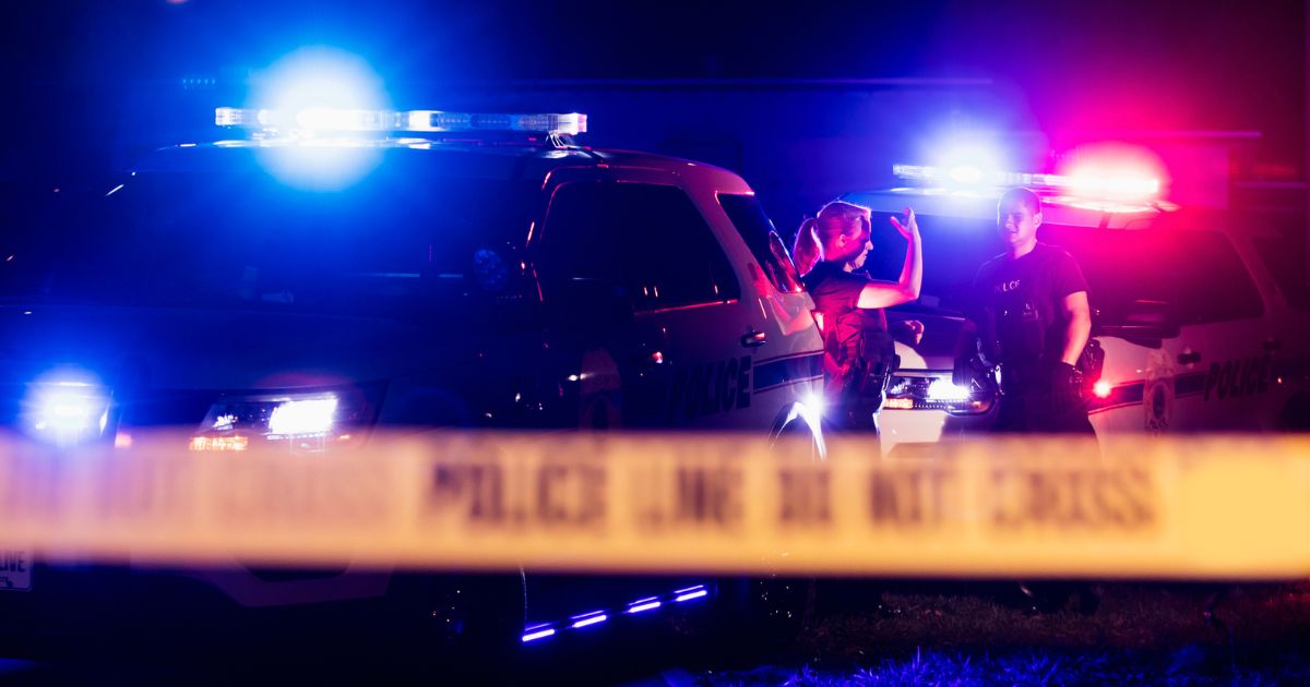 This Getty stock image shows police officers at night, behind police tape that is shown in the foreground.