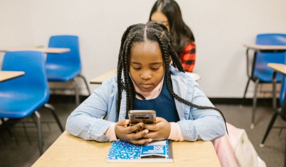 This image shows a young student sitting at her desk, using a smartphone.