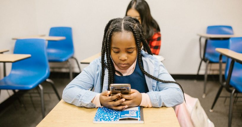 This image shows a young student sitting at her desk, using a smartphone.