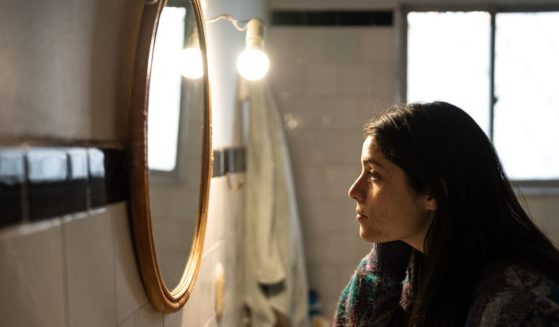 This stock image shows a woman looking at herself in the mirror.