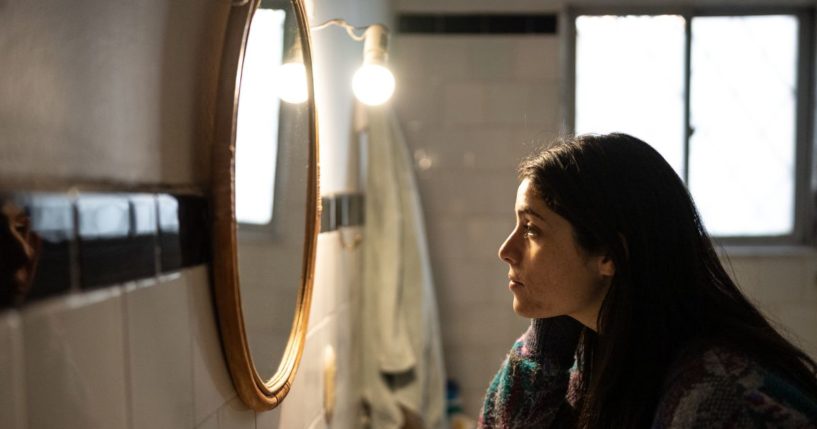 This stock image shows a woman looking at herself in the mirror.