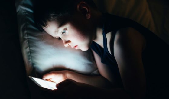 A young boy looks at a tablet or smartphone at night in bed.