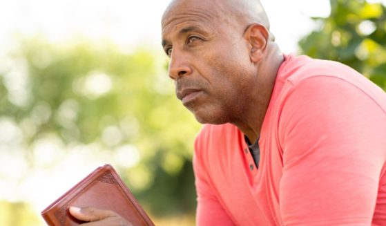 This image shows a man sitting, leaning forward, with his elbows on his knees and a book in his hands. He appears to be contemplating what he just read.