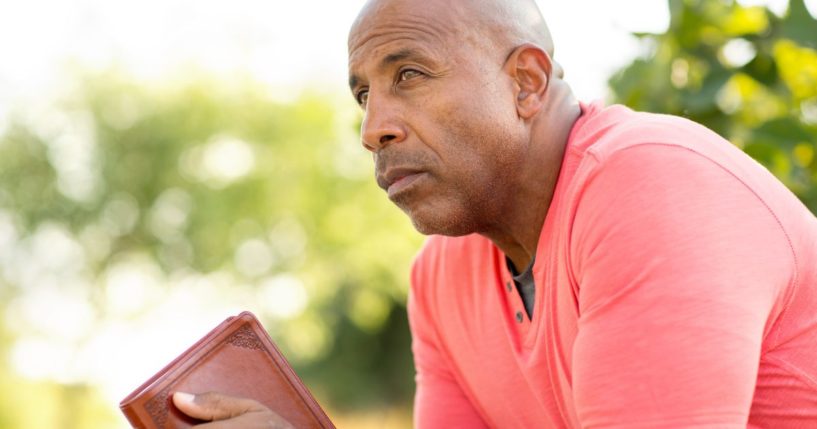 This image shows a man sitting, leaning forward, with his elbows on his knees and a book in his hands. He appears to be contemplating what he just read.