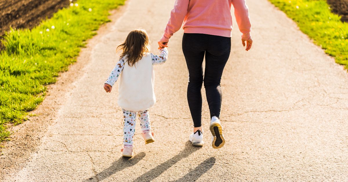 This image shows a mother and child walking on a countryside road between two agricultural fields.