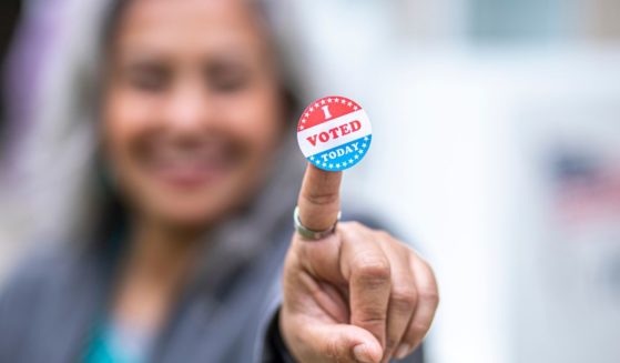 This image shows a close-up of an "I voted sticker" that a senior woman is holding up. Her face is blurred.