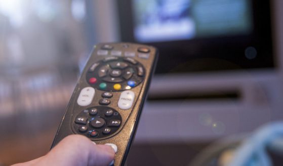 A stock photo shows a man watching television using a TV remote control.