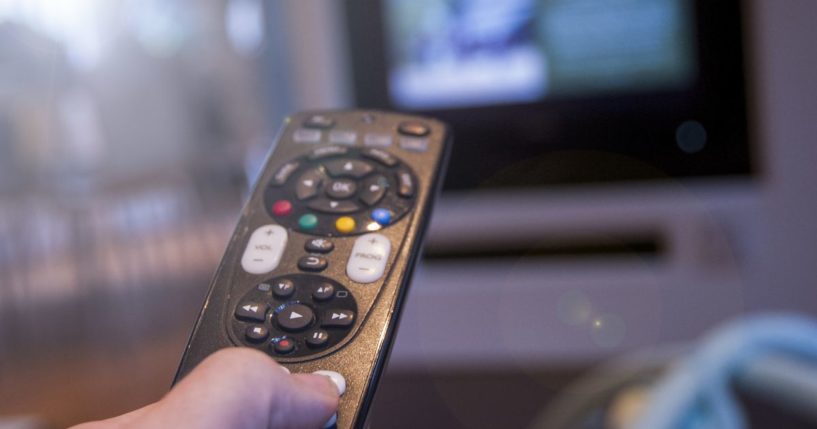 A stock photo shows a man watching television using a TV remote control.