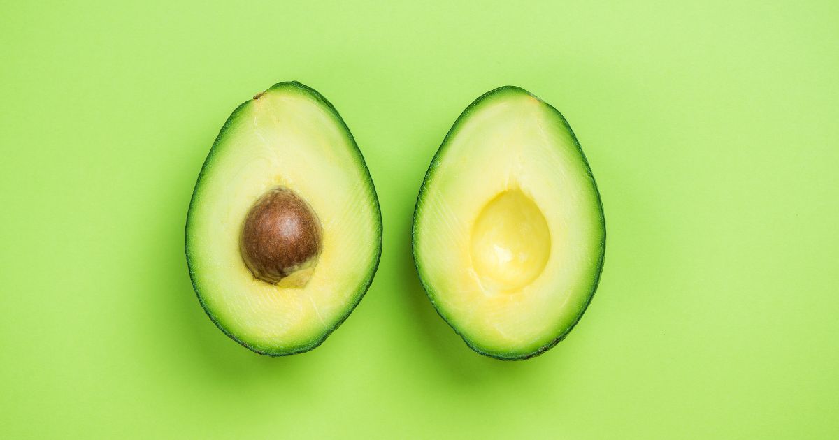 This image shows an avocado cut in half displayed on a bright green background.