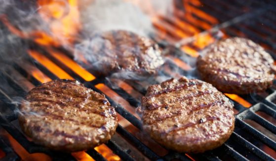A stock photo shows burgers cooking on a hot grill with flames.
