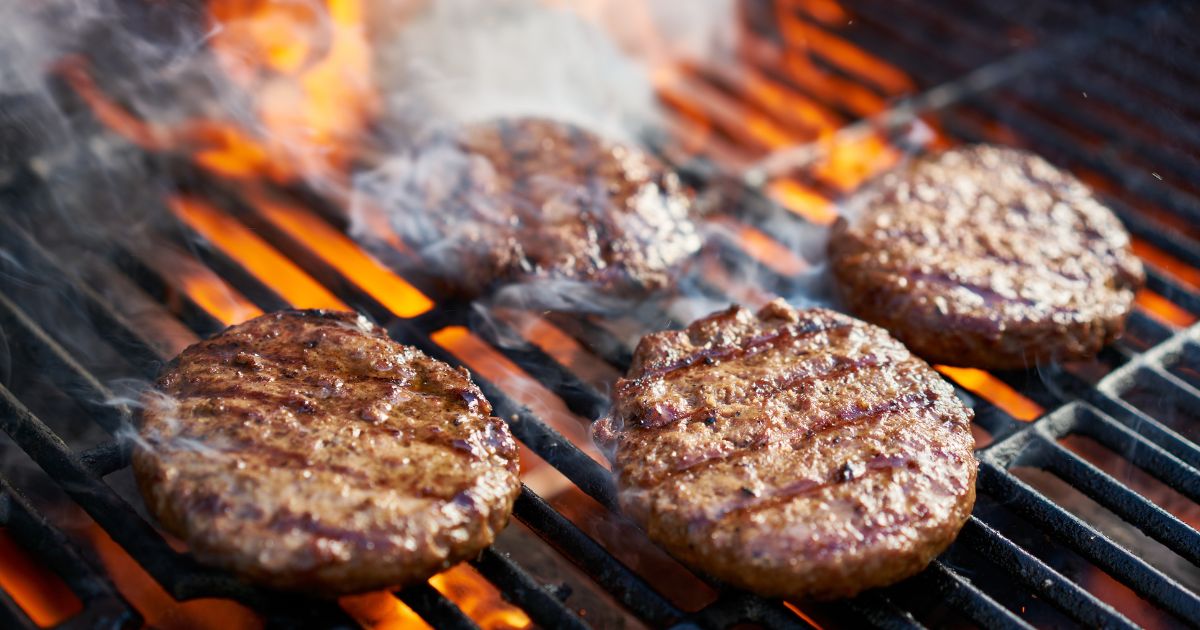 A stock photo shows burgers cooking on a hot grill with flames.
