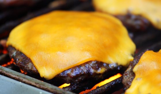 This image shows cheeseburgers cooking on an outdoor grill.