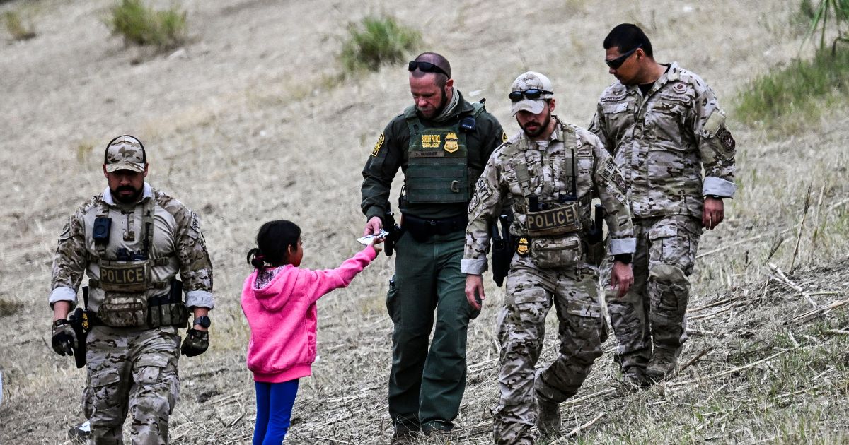 A US Customs and Border Protection officer gives food to an immigrant child waiting to be processed at a US Border Patrol transit center after crossing the border from Mexico at Eagle Pass, Texas on December 22, 2023.