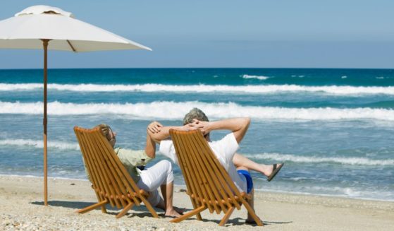 This image shows a retired couple sitting in chairs next to an umbrella on the beach.