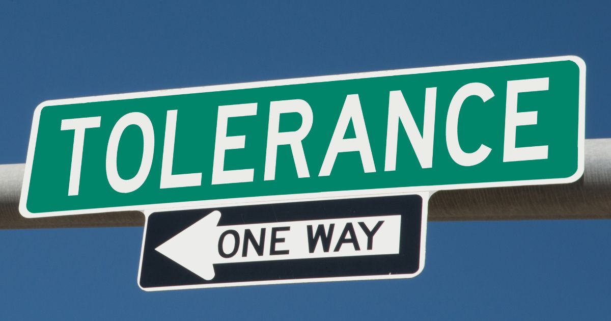 This image shows the word tolerance printed on a green overhead highway sign with a one way arrow sign attached below it.