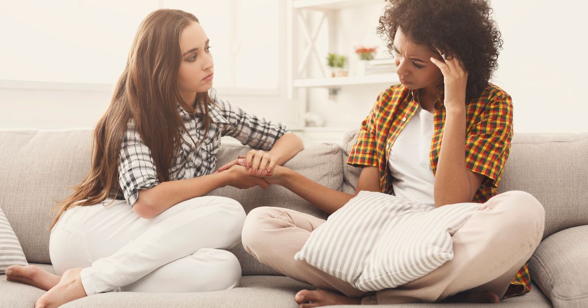 This image shows two young women talking about problems at home. One friend is holding the other's hand to console her.