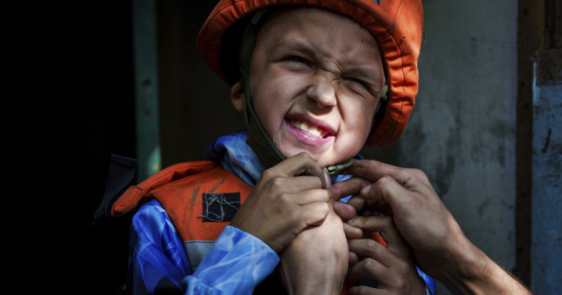 A Fenix team rescue worker places a helmet on Bohdan Scherbyna, 9, as he is evacuated with his mother Maryna Scherbyna and 14 year old sister Angelina Scherbyna, as local people as moved from Selidove to safe areas, in Pokrovsk, Donetsk region, Ukraine, on Tuesday.