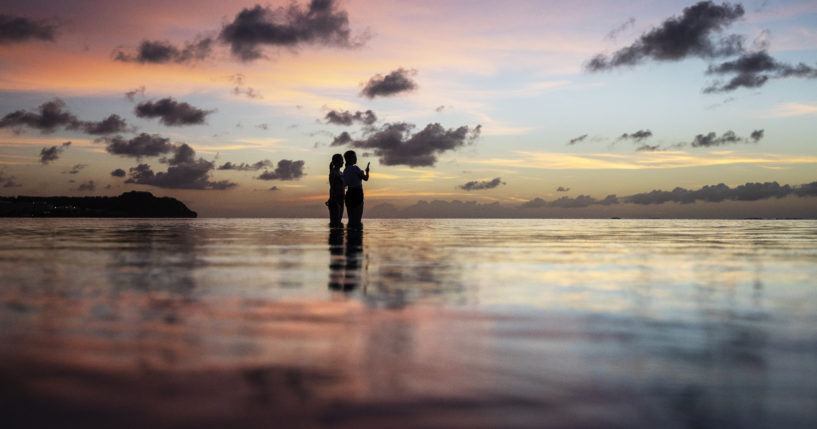 Tourists watch the sun set along a popular beach in Tamuning, Guam, May 6, 2019.