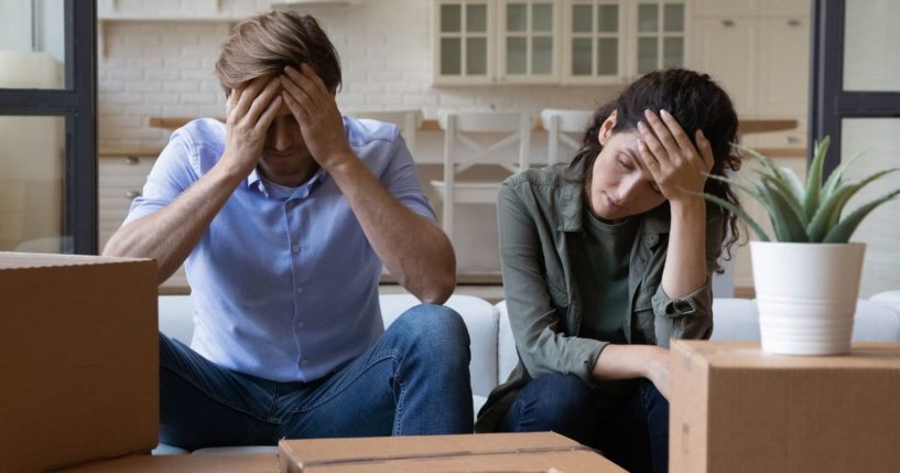 An exhausted young couple sits on a couch in this stock photo.