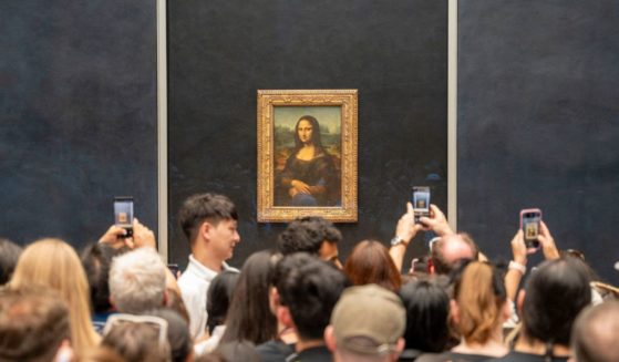 Crowd of tourists with their phones in hand, taking photos of Leonardo da Vinci's Mona Lisa.