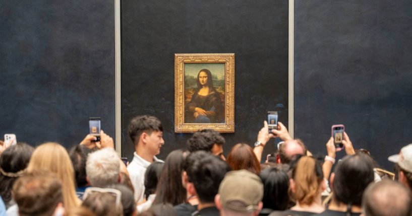 Crowd of tourists with their phones in hand, taking photos of Leonardo da Vinci's Mona Lisa.