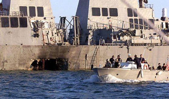 U.S. Navy and Marine Corps security personnel patrol past the damaged U.S. Navy destroyer USS Cole in Yemen on Oct. 18, 2000.