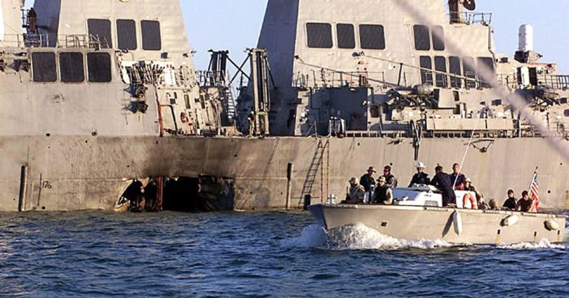 U.S. Navy and Marine Corps security personnel patrol past the damaged U.S. Navy destroyer USS Cole in Yemen on Oct. 18, 2000.