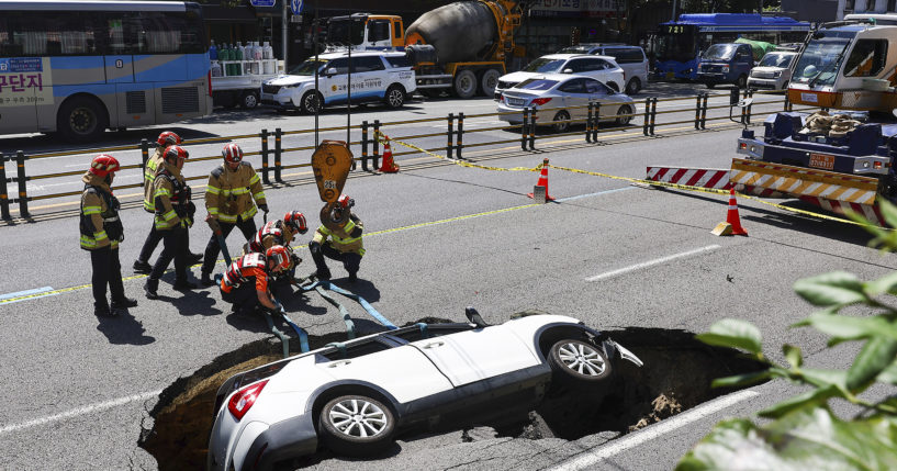 South Korean firefighters prepare to lift a vehicle that fell into a sinkhole on a street in Seoul, South Korea, Thursday, August 29, 2024.