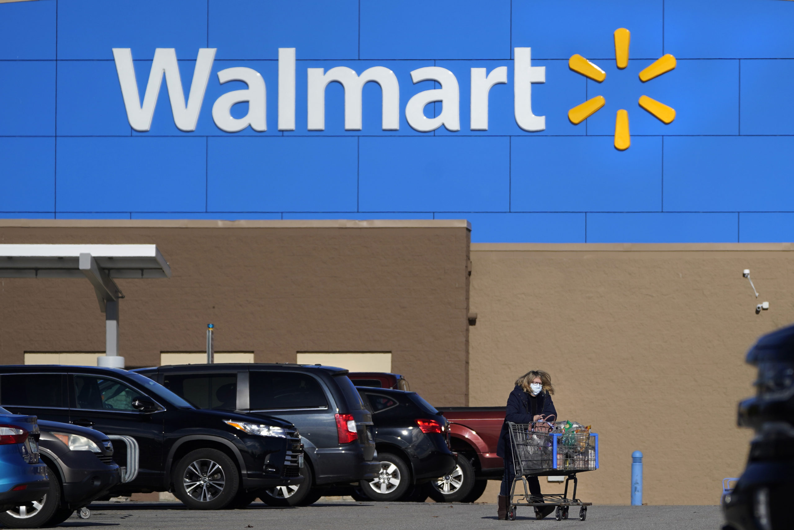 A woman wheels a cart with her purchases out of a Walmart store, November 18, 2020, in Derry, New Hampshire.