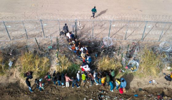 In an aerial view, immigrants pass through coils of razor wire while crossing the U.S.-Mexico border on March 13, 2024 in El Paso, Texas.