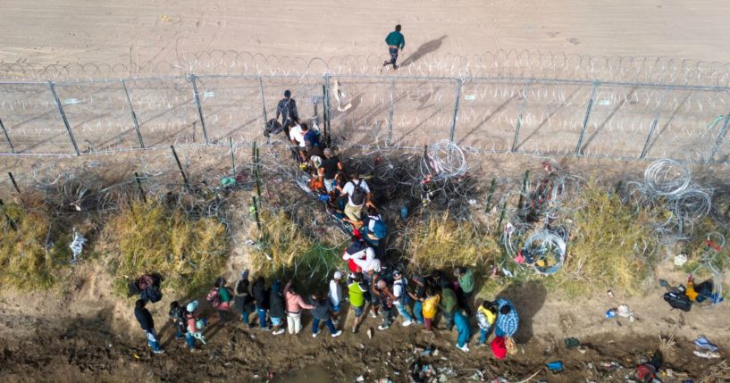 In an aerial view, immigrants pass through coils of razor wire while crossing the U.S.-Mexico border on March 13, 2024 in El Paso, Texas.