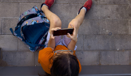 An 11-year-old boy plays with his father's phone outside school in Barcelona, Spain, Monday, June 17, 2024.