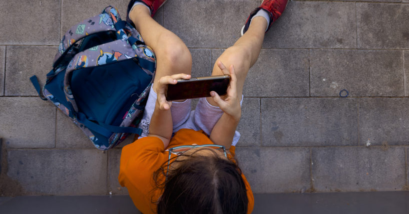 An 11-year-old boy plays with his father's phone outside school in Barcelona, Spain, Monday, June 17, 2024.